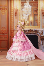 Doll in a pink and white dress standing in an ornate room with a chandelier.