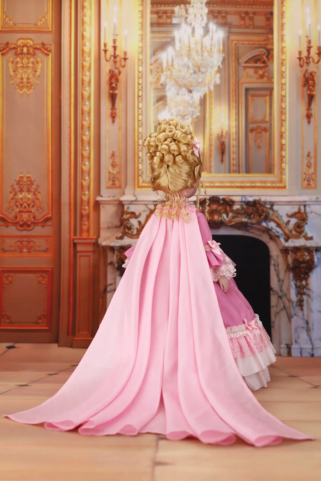 Doll in a pink dress standing in an ornate room with a chandelier.