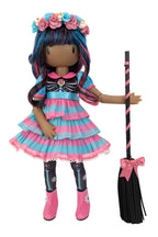 A Gorjuss doll with long blue and pink hair wearing a pink and blue striped dress, floral headband, and black tights, standing beside a black broom with pink stripes and a pink bow, on a white background.