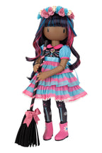A Halloween-themed doll with long dark hair featuring pink and blue streaks, wearing a pink and blue striped dress, black tights with skeleton details, pink boots, and a flower crown, holding a black broom with a pink bow.