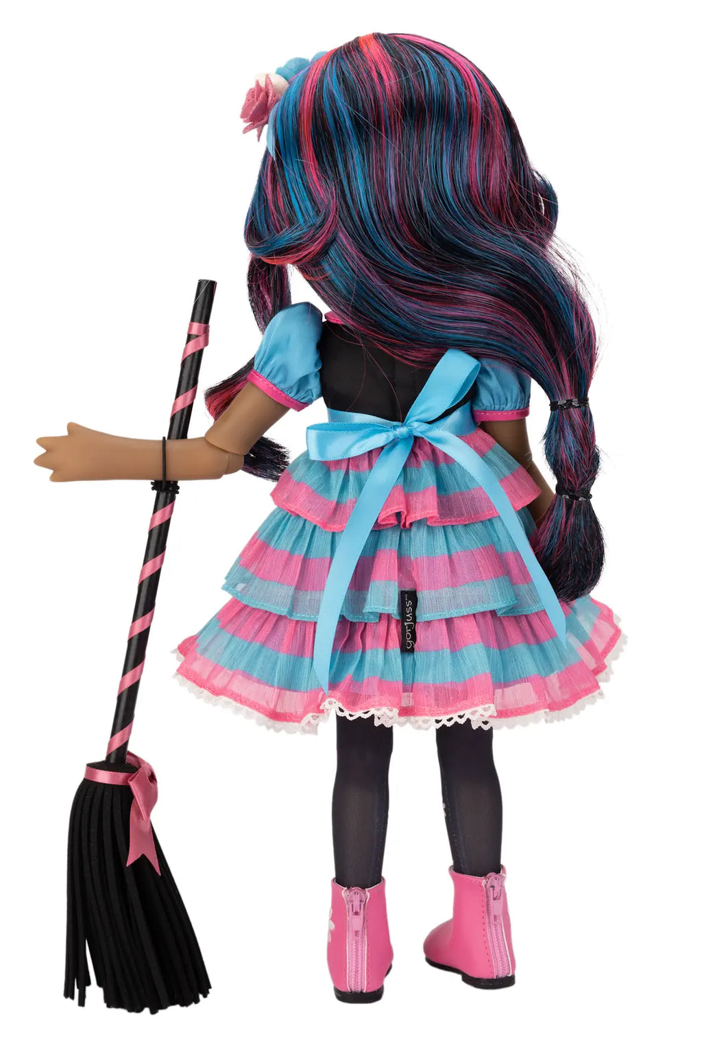 A doll shown from the back wearing a tiered pink and blue dress, black tights, and pink boots, holding a black broom with pink stripes against a white background.