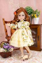 Doll in a floral dress standing in a decorative setting with flowers and a chair.