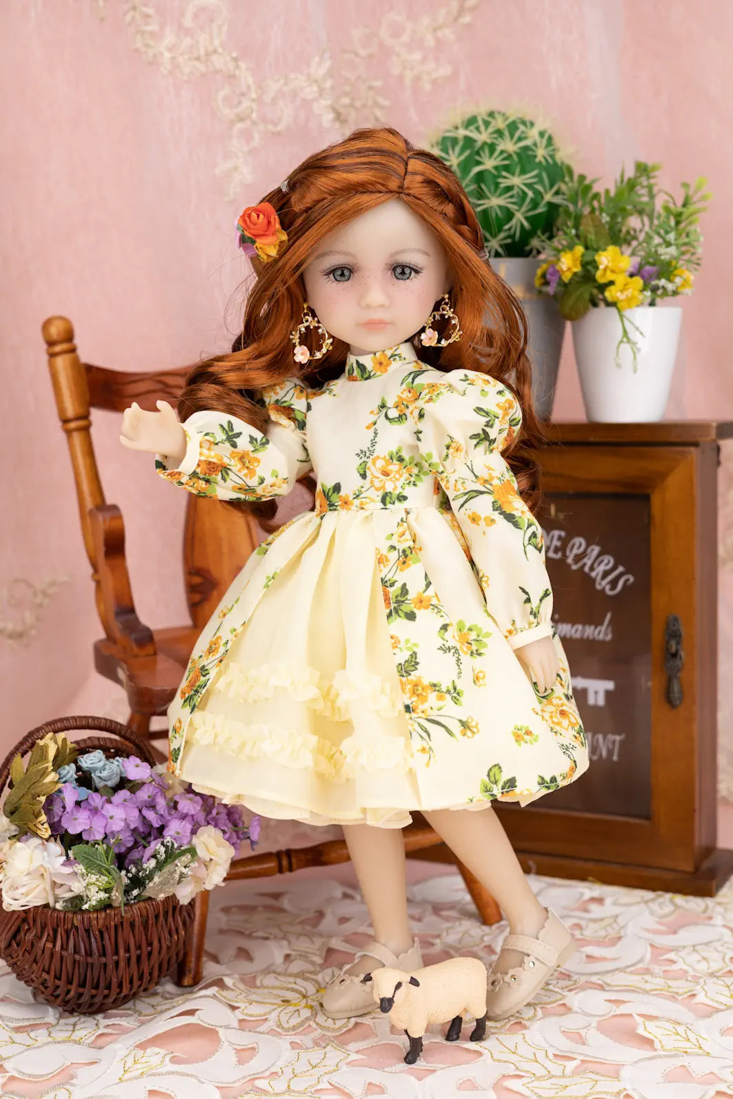Doll in a floral dress standing in a decorative setting with flowers and a chair.