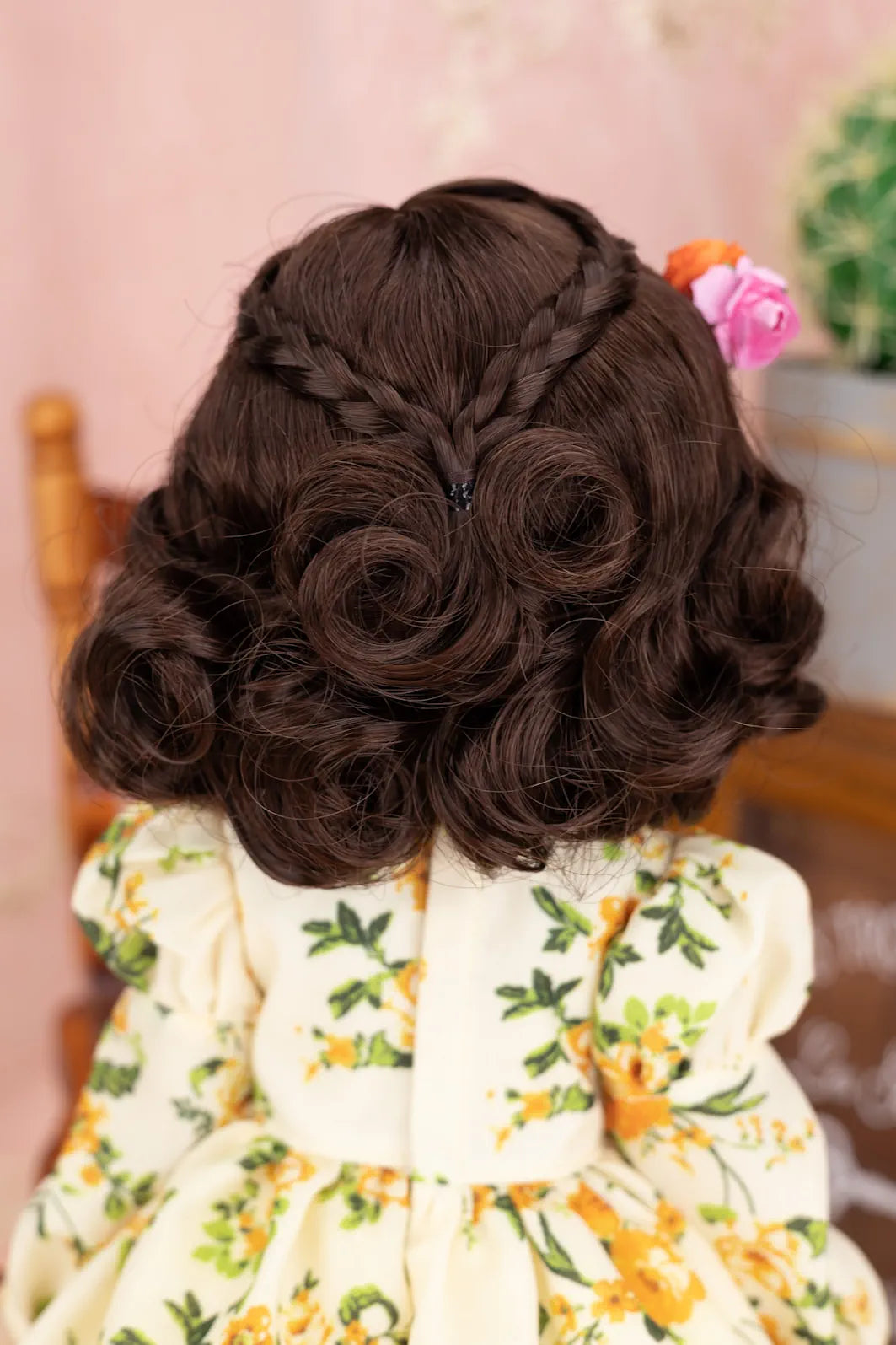 Back view of a doll with styled hair and a floral dress, sitting indoors.