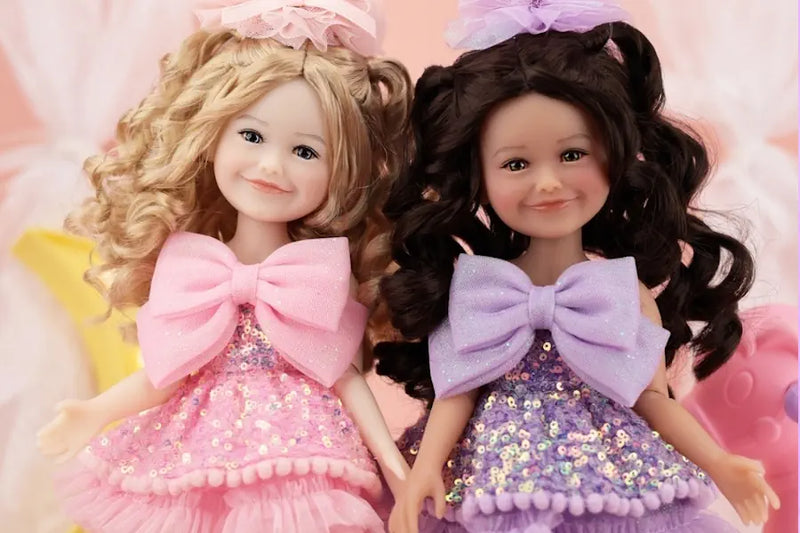 Two Gift Edition Siblies dolls with large bows on their dresses against a soft pink background