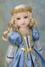 A close-up of a blonde doll wearing a light blue gown with gold trim, a pearl necklace, and a gold crown with blue stones, set against a soft blue background.