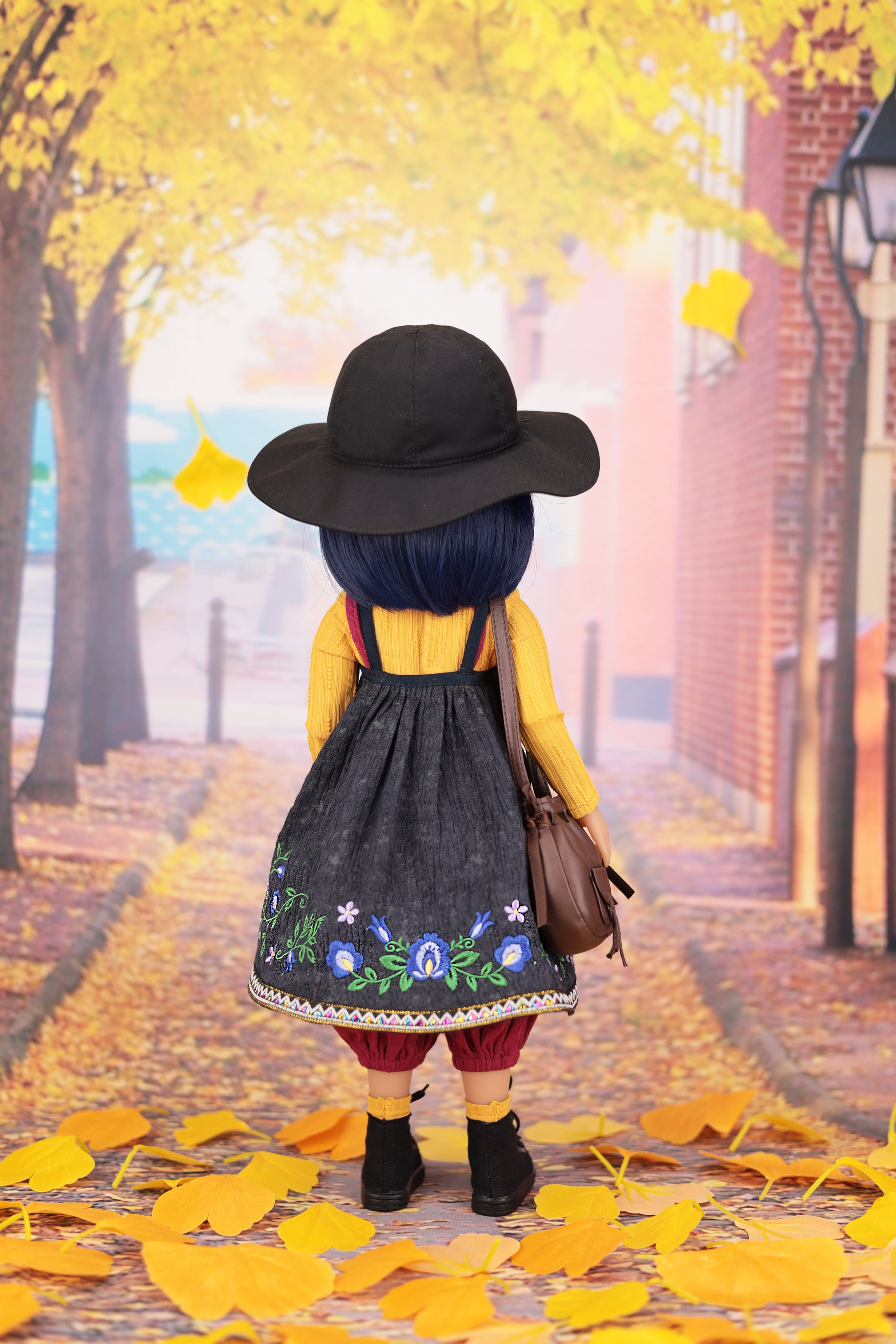 Person wearing a black hat and yellow coat walking down a street with yellow leaves on the ground.
