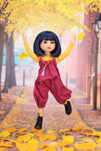 Doll in a yellow top and red outfit standing on a path with yellow leaves