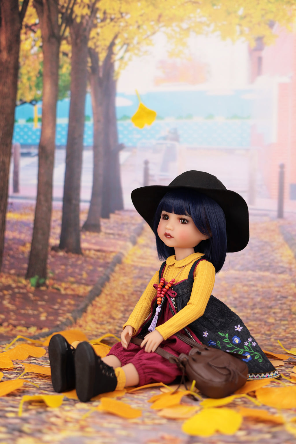 Doll sitting on a path with autumn leaves and trees in the background