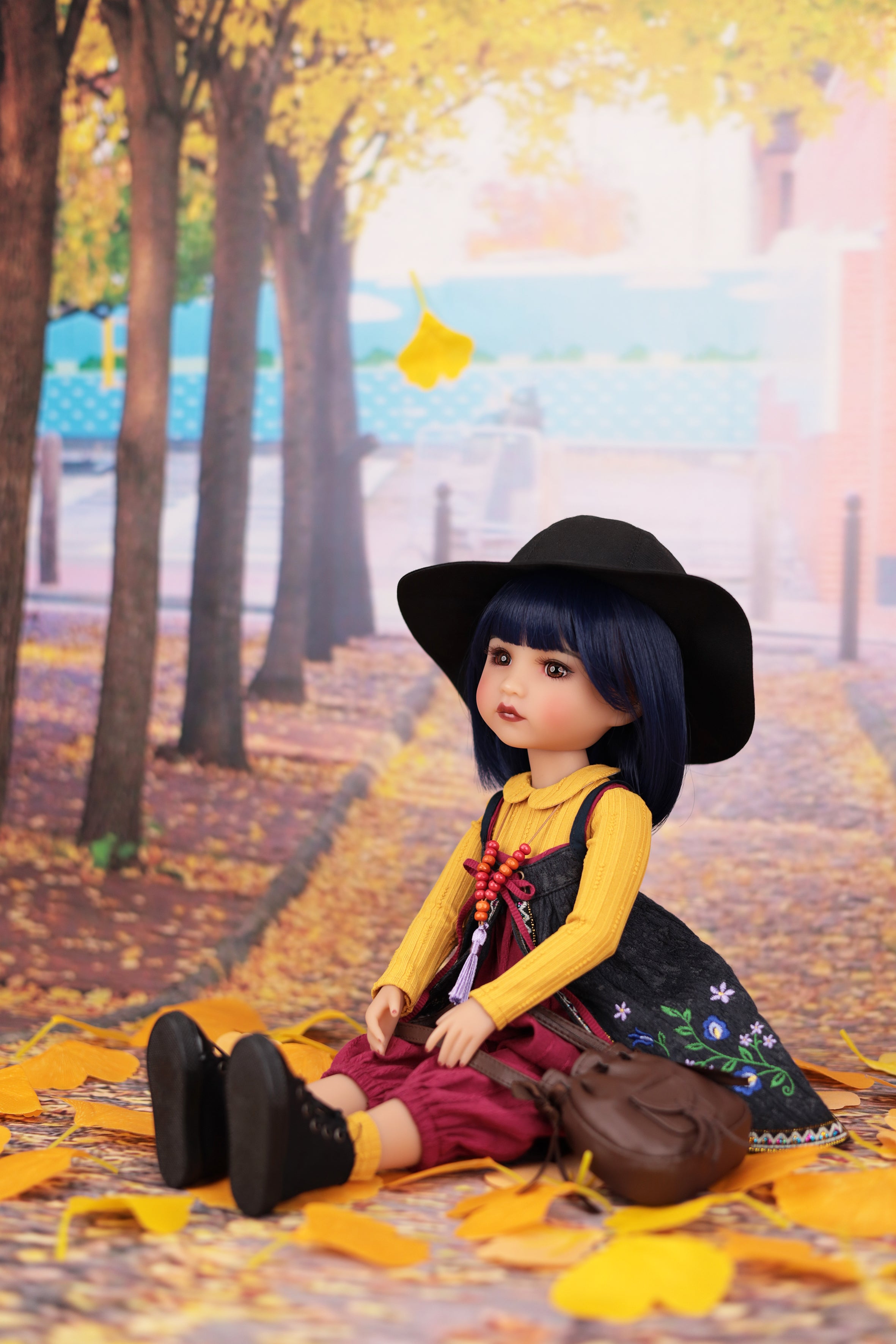 Doll sitting on a path with autumn leaves and trees in the background