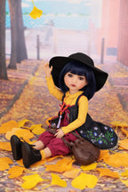 Doll sitting on autumn leaves with a black hat and yellow sweater