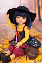 Doll with black hat and yellow outfit sitting on autumn leaves