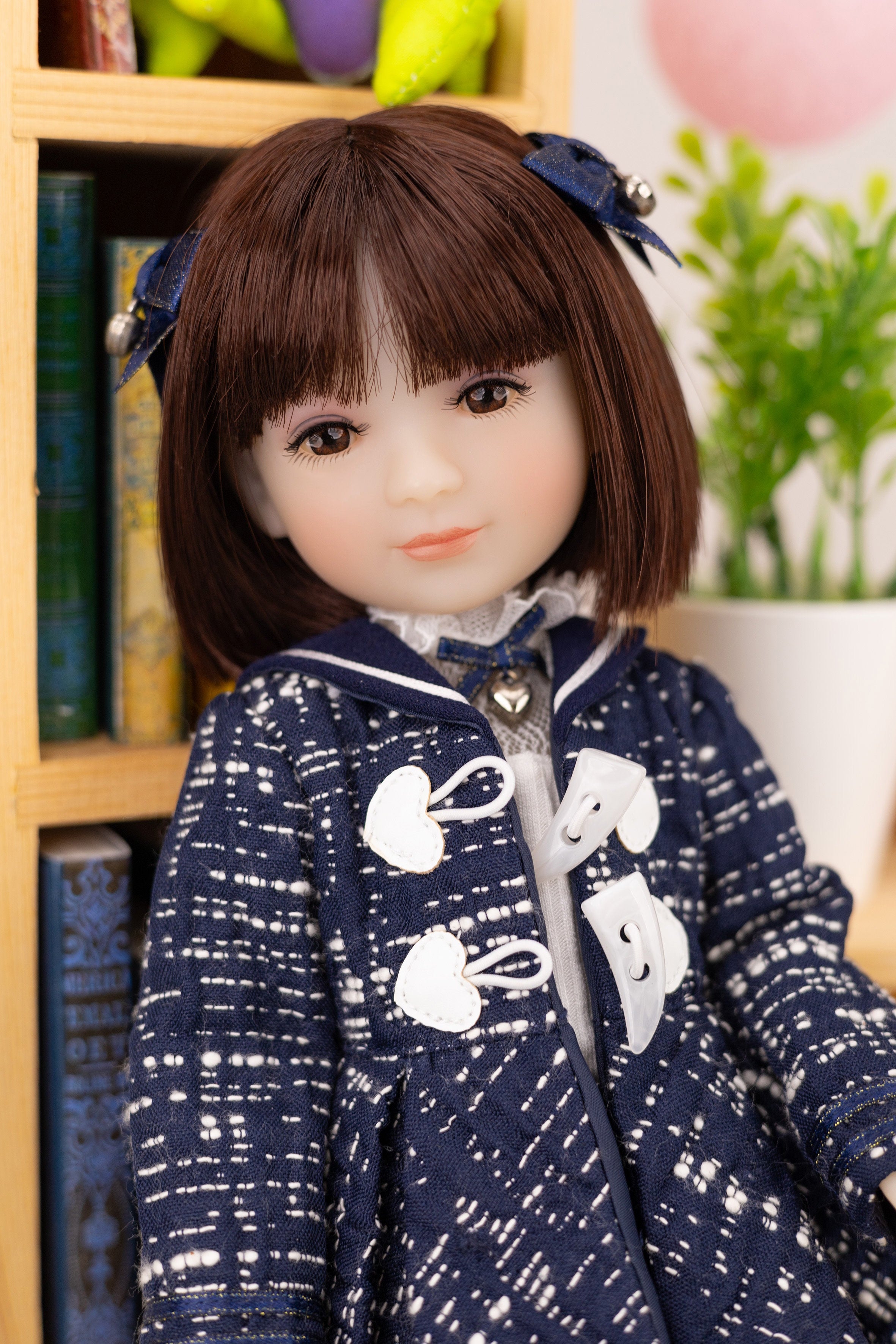 Doll with a navy blue outfit featuring white patterns, sitting in front of a bookshelf.
