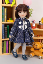 Doll in a blue coat standing next to a teddy bear in a room with books and toys.