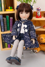 Doll in a blue outfit sitting on a chair with a bookshelf and toys in the background