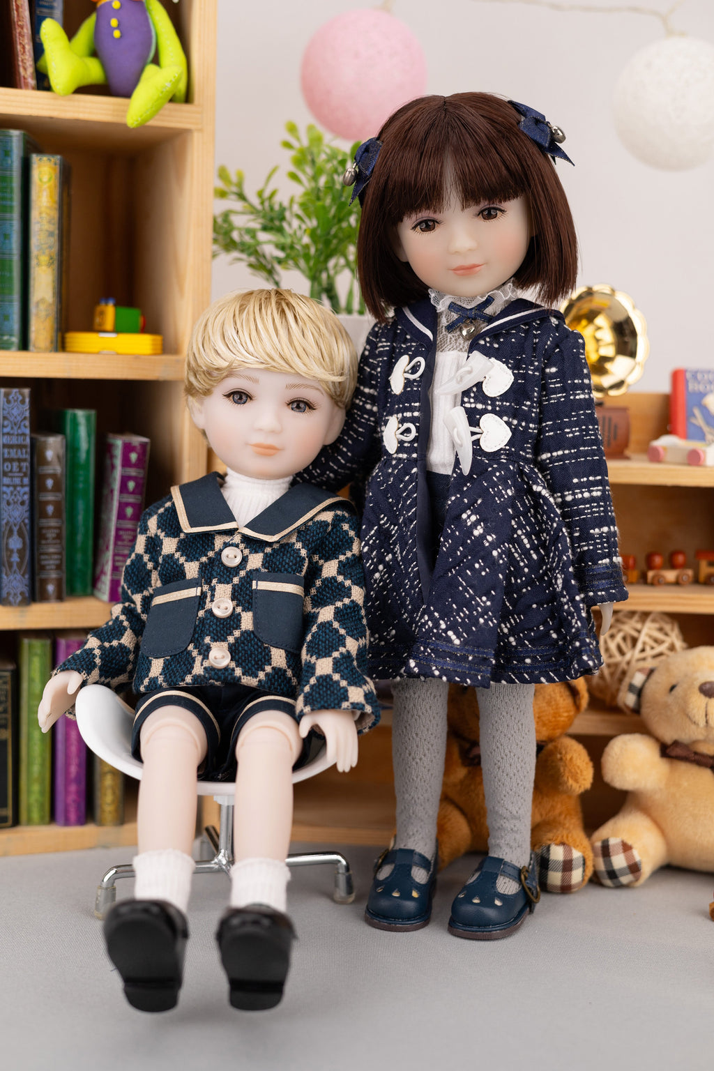 Two dolls in matching outfits standing in a room with books and toys.