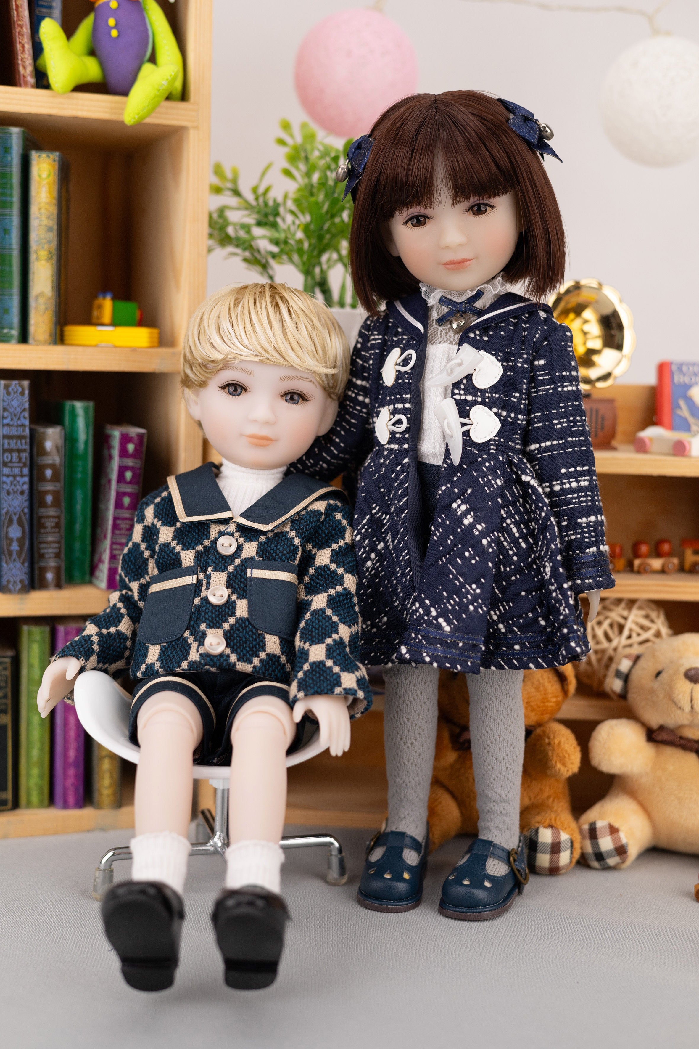 Two dolls in matching outfits standing in a room with books and toys.
