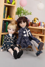 Two dolls in school uniforms sitting on a chair in front of a bookshelf.