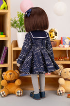 Doll wearing a navy blue dress with white patterns in a room with toys and books.