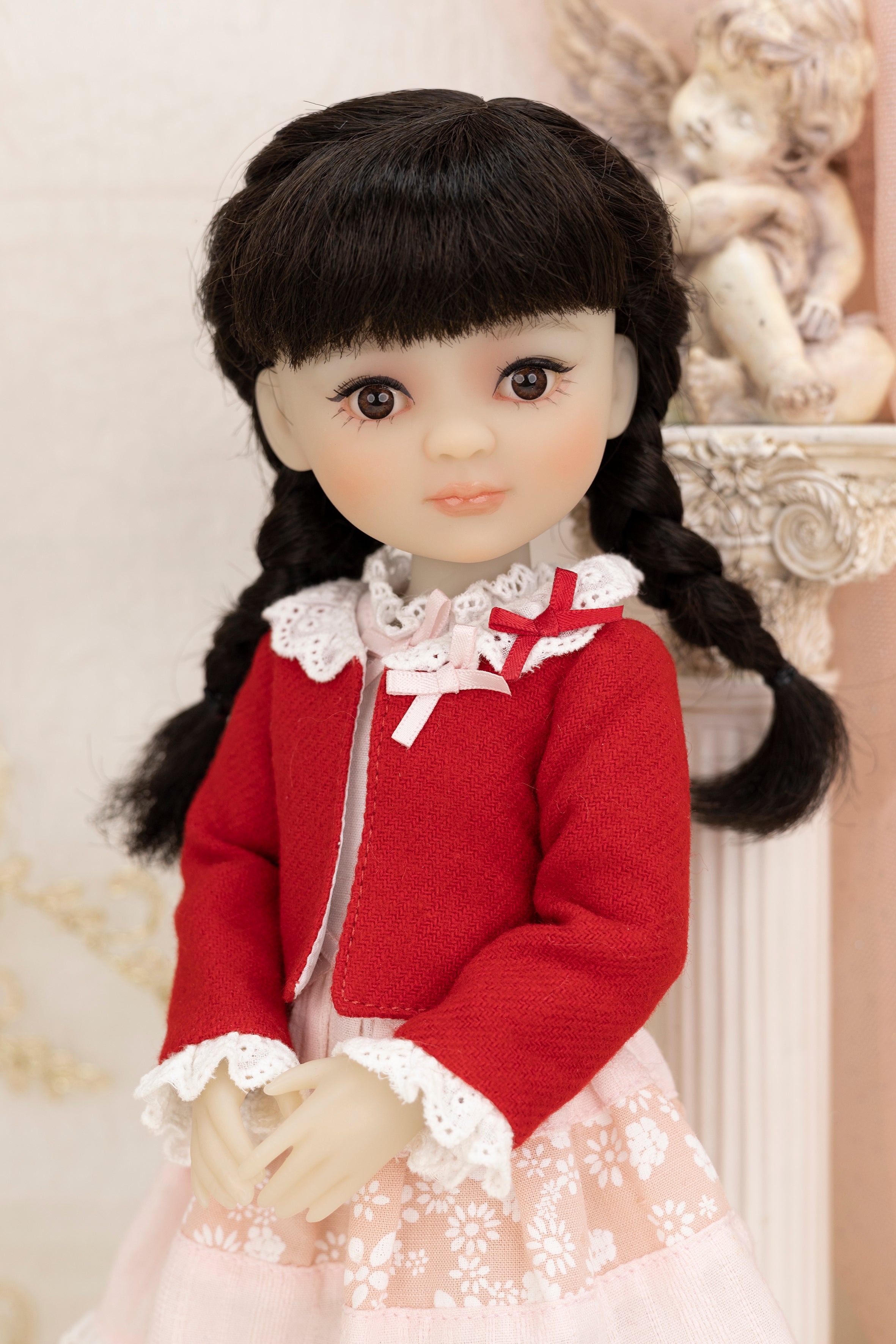 Doll with black hair styled in pigtails, wearing a red jacket and white dress.