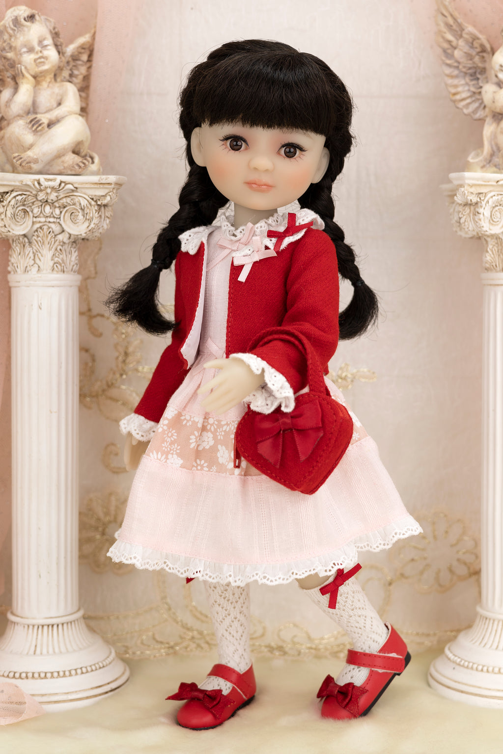 Doll in a red and white outfit standing between two decorative columns.