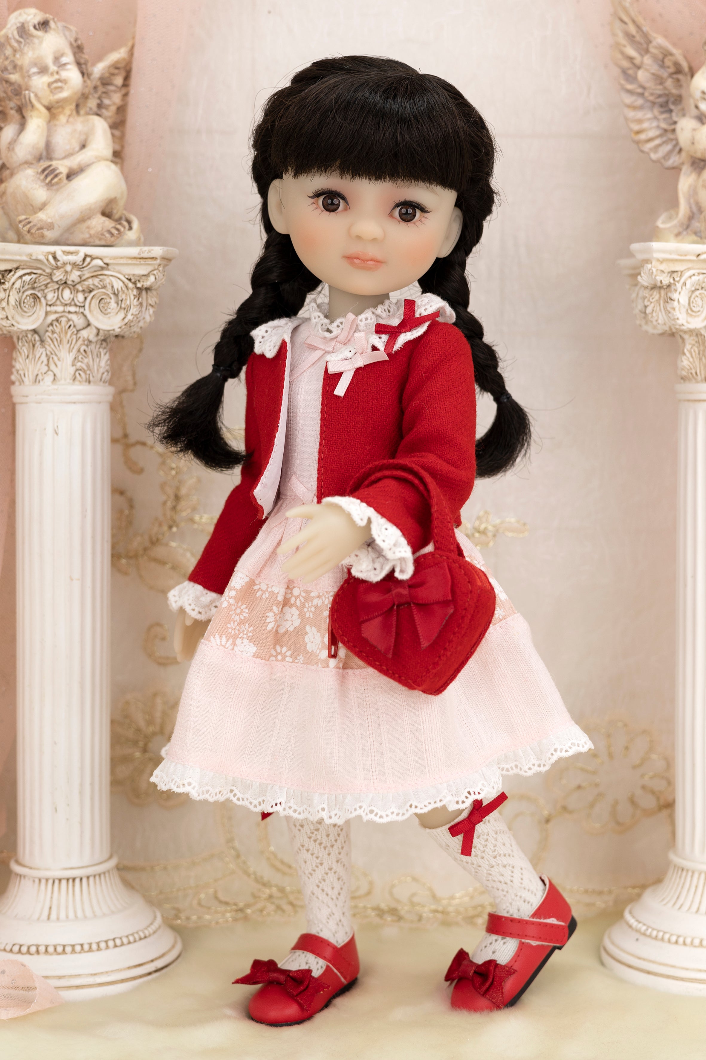 Doll in a red and white outfit standing between two decorative columns.
