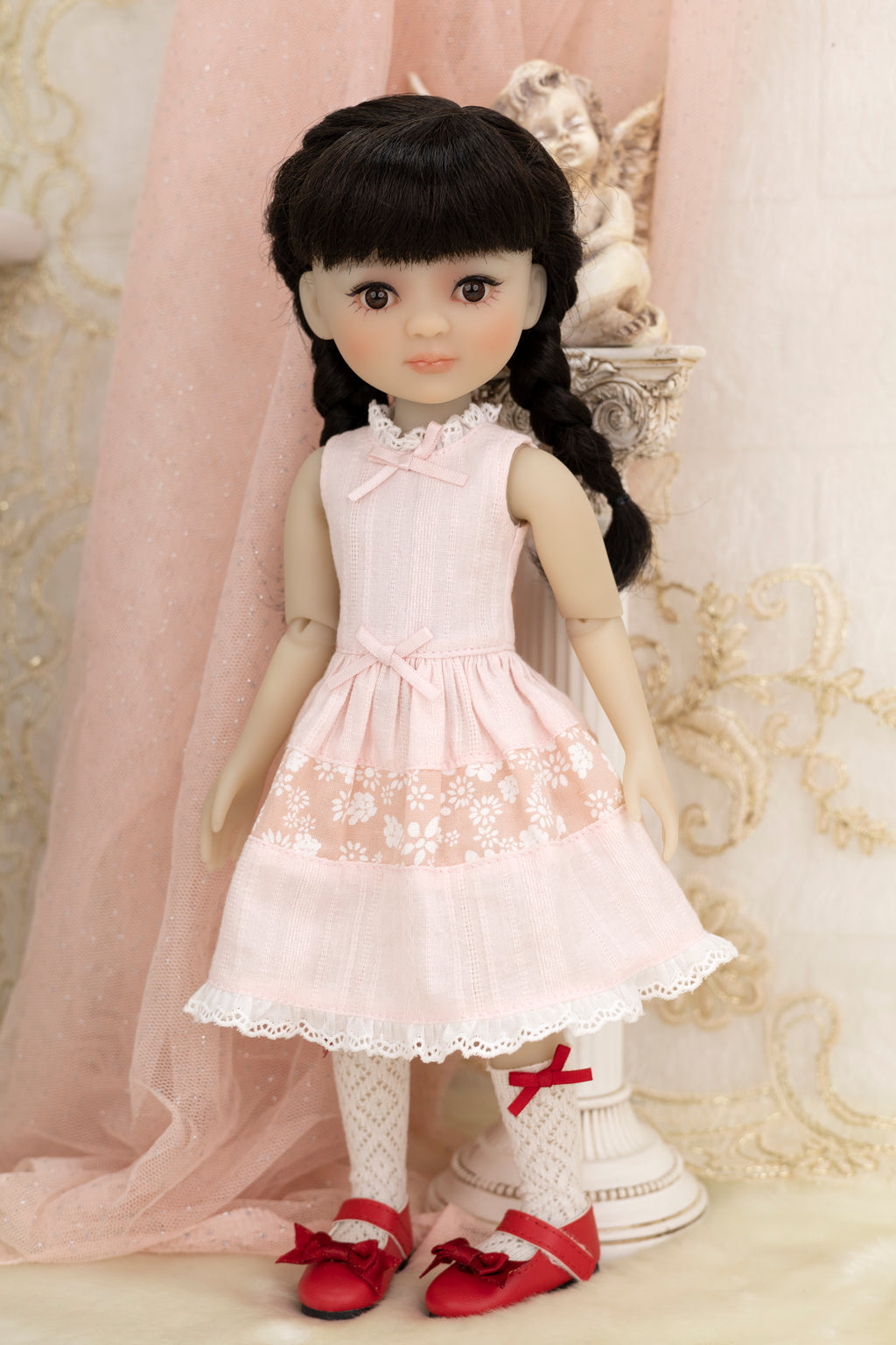 Doll wearing a white dress with lace details and red shoes in a decorative setting