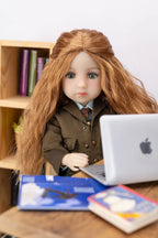 Doll with long brown hair sitting at a desk with a laptop and books.