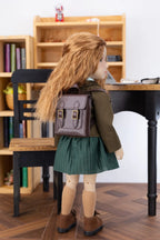 Doll with a backpack in a room with a bookshelf and desk.