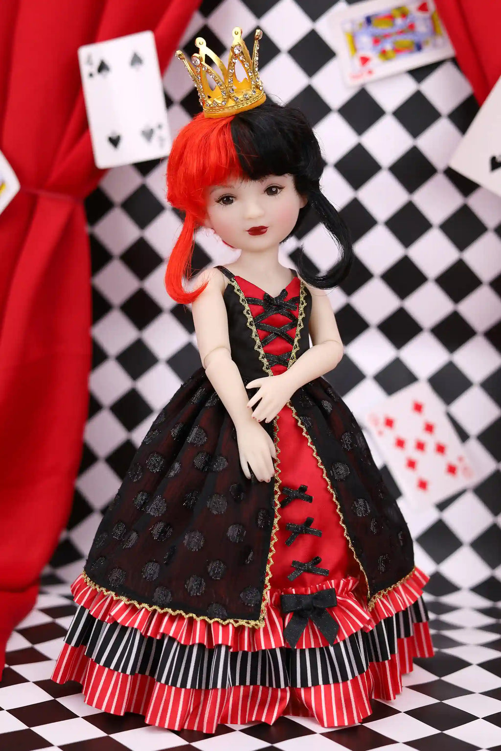 Doll with red hair and a black and red dress in front of a checkered background with playing cards.