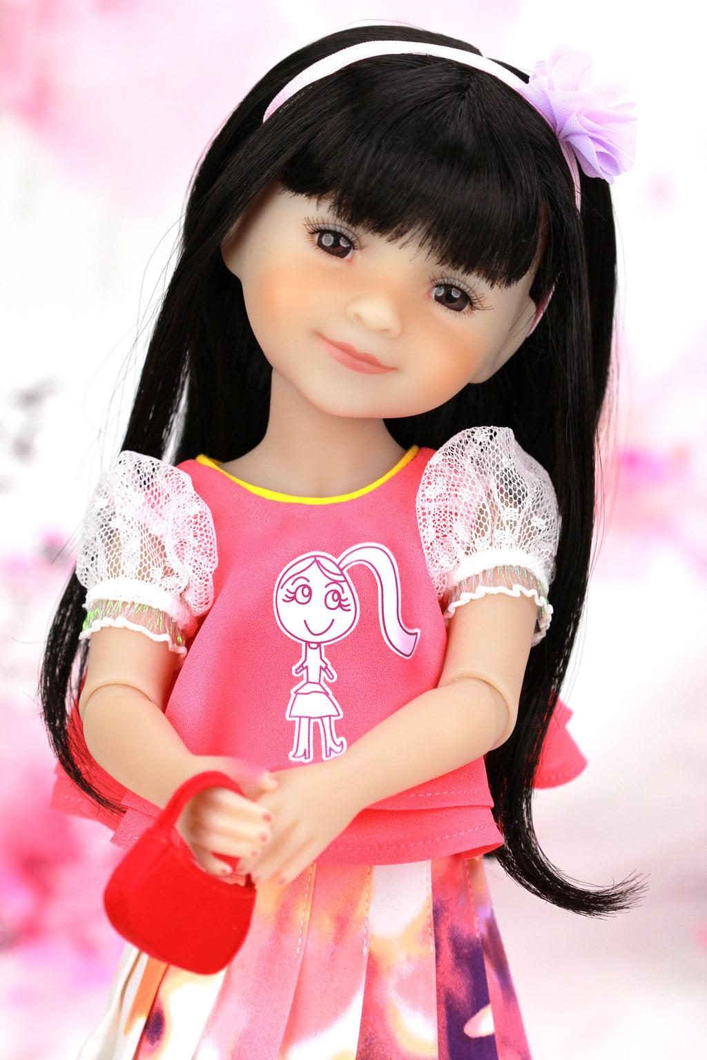 Child-like doll with long black hair and a pink outfit against a soft pink background