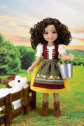 A doll with curly brown hair stands in a stylized outdoor farm scene, wearing a traditional dirndl dress with white sleeves, a burgundy bodice, olive green apron, yellow skirt, and brown lace-up boots. The doll holds a small silver bucket and stands beside a wooden fence with a white sheep toy.