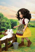 A doll with long curly brown hair stands beside a small wooden fence in a stylized outdoor farm scene, reaching toward a white plush lamb while wearing a traditional-style dress with a yellow skirt, green apron, and brown boots.