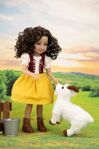 A doll with curly brown hair wearing a yellow dress and brown boots, standing beside a small white plush lamb toy in a stylized outdoor farm scene with a sunset sky.