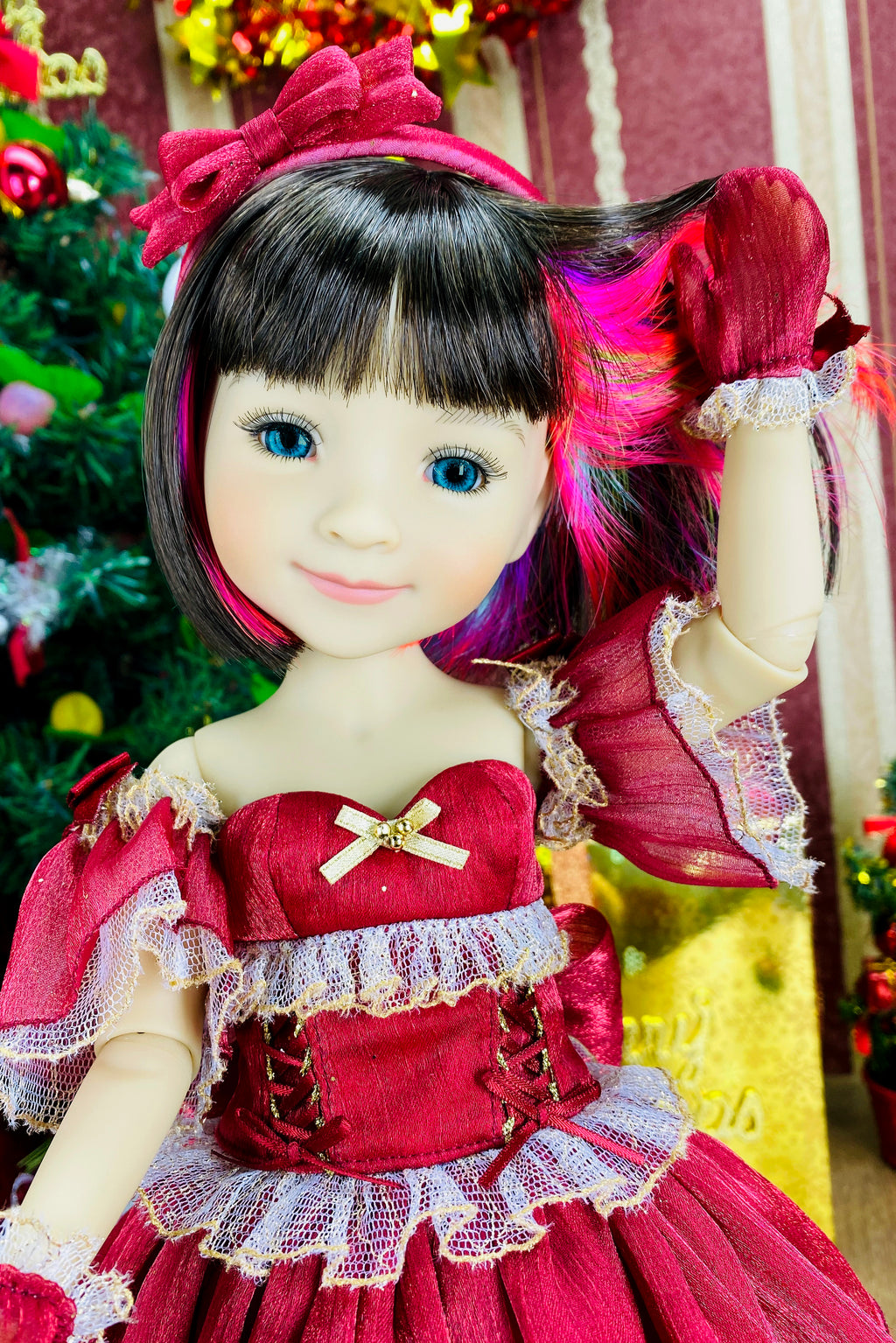 Doll in a red dress with decorative elements, standing in front of a decorated Christmas tree.