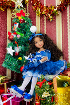 Doll in a blue dress standing next to a decorated Christmas tree with presents.