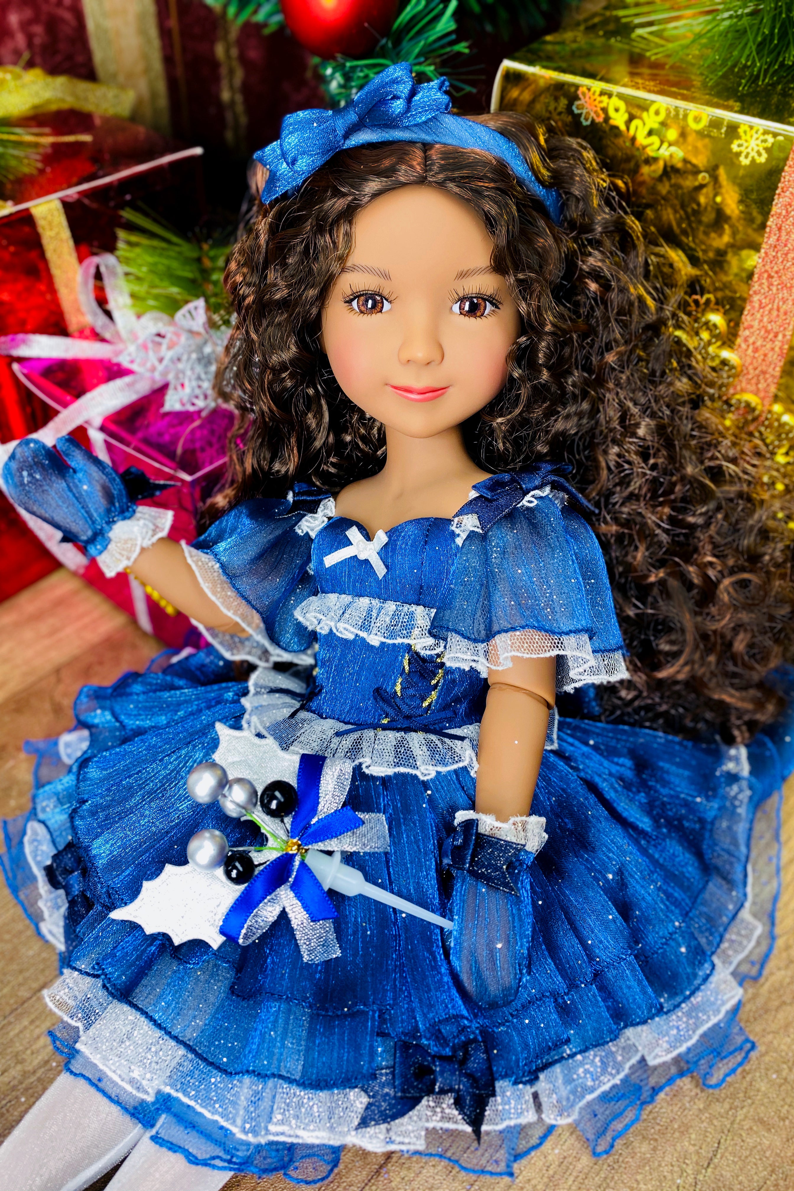 Doll in a blue dress with a bow headband, surrounded by festive decorations.