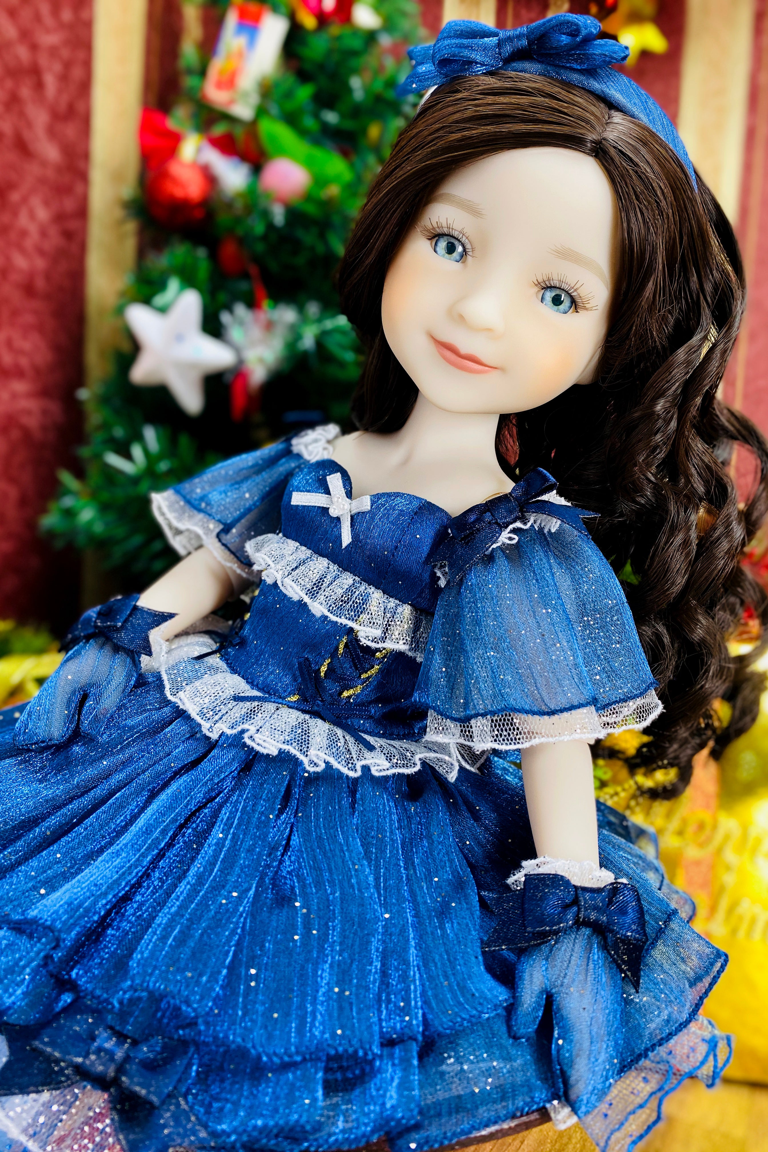 Doll in a blue dress with a Christmas tree in the background