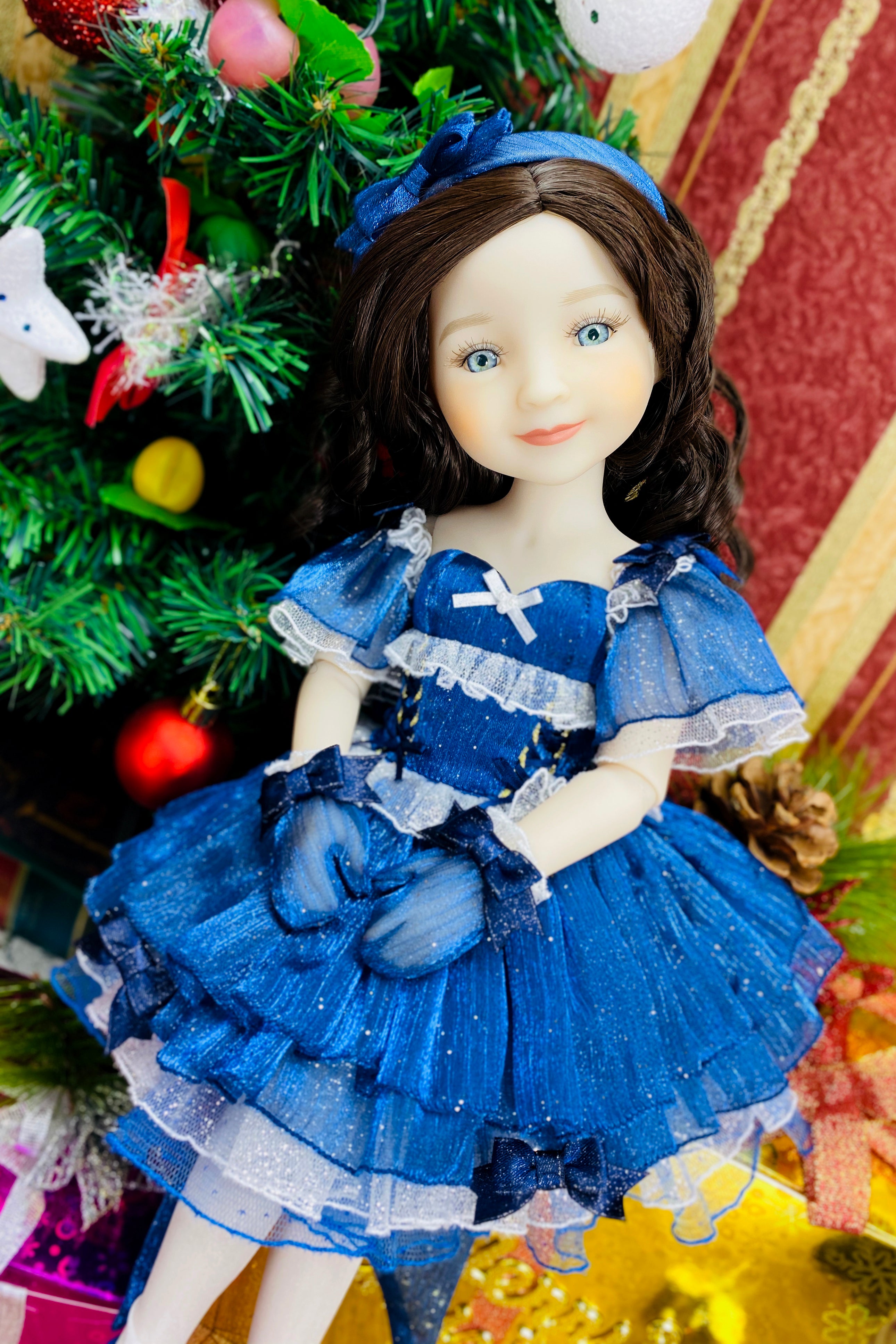 Doll in a blue dress with a Christmas tree in the background