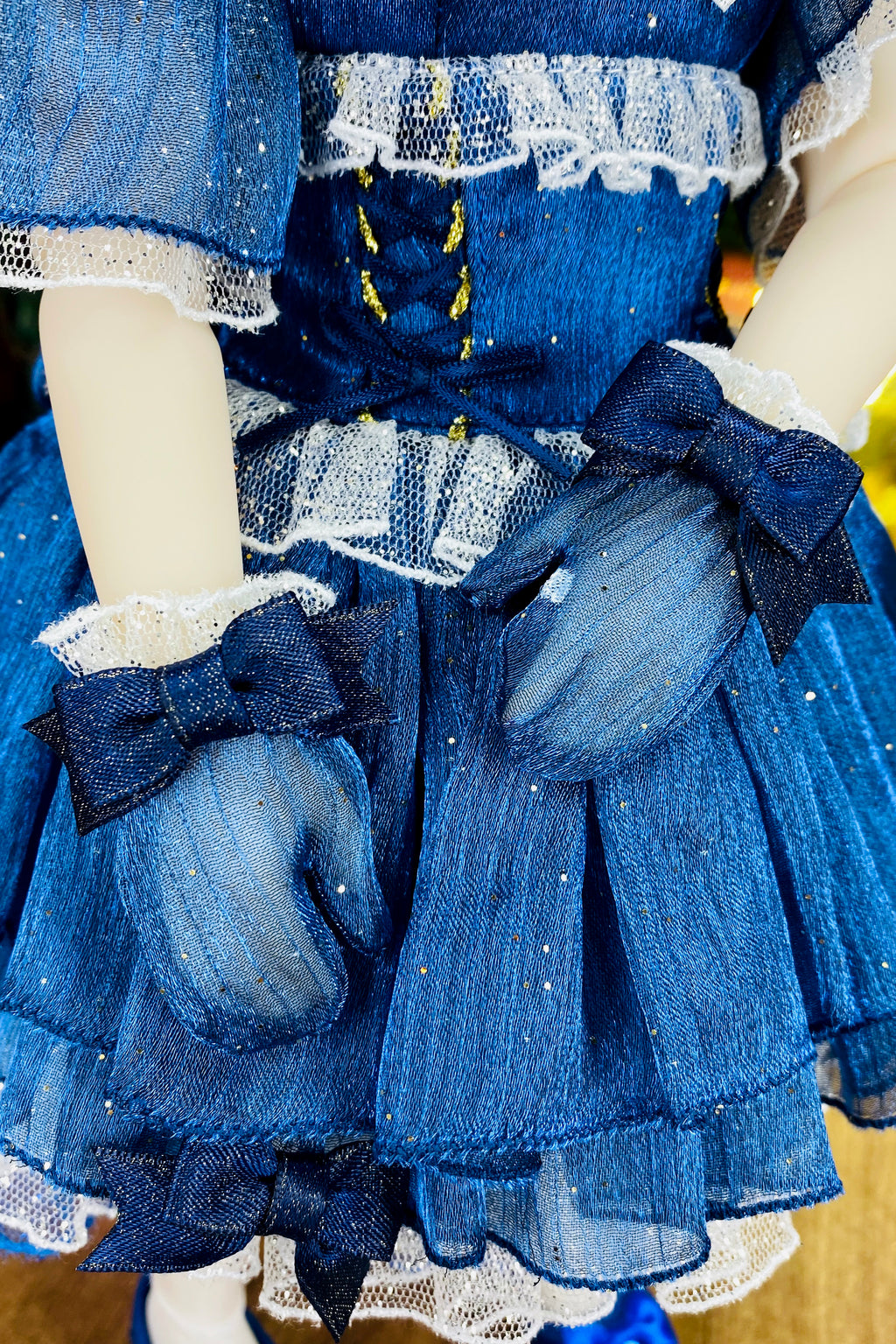 Close-up of a doll wearing a blue dress with lace details and gloves.