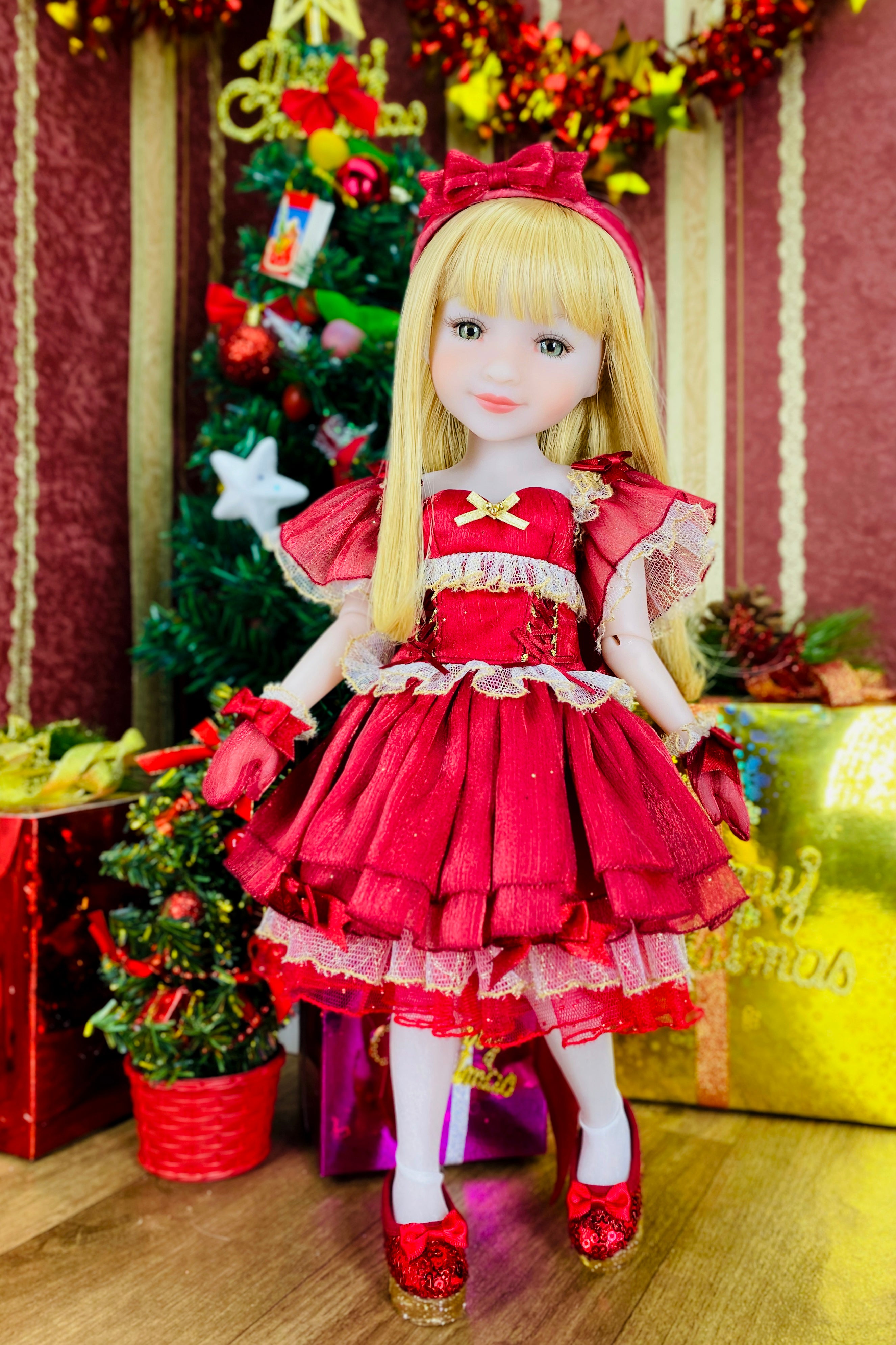 Doll in a red dress standing in front of a decorated Christmas tree.