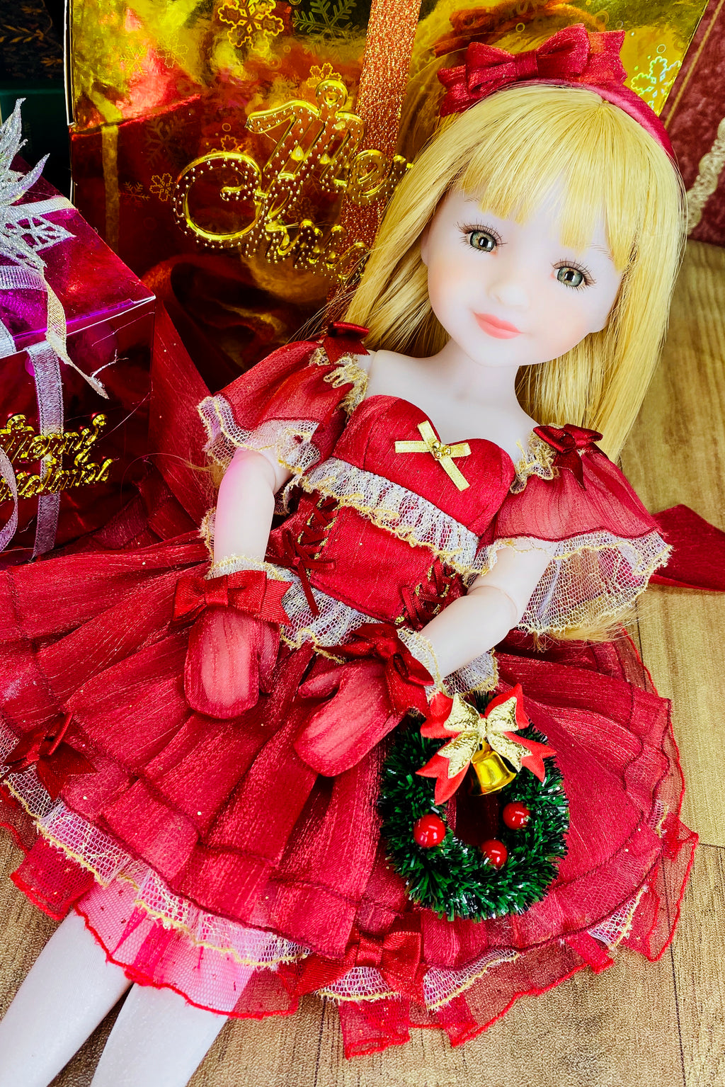 Doll in a red dress with a Christmas wreath, surrounded by festive decorations.