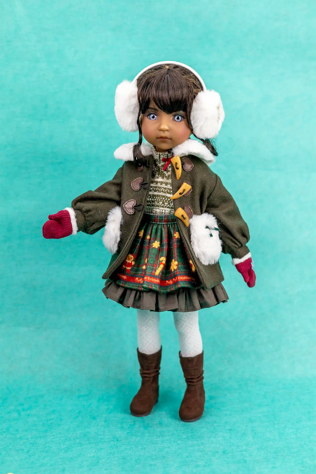 Doll wearing a winter outfit with a coat, skirt, boots, and earmuffs on a teal background