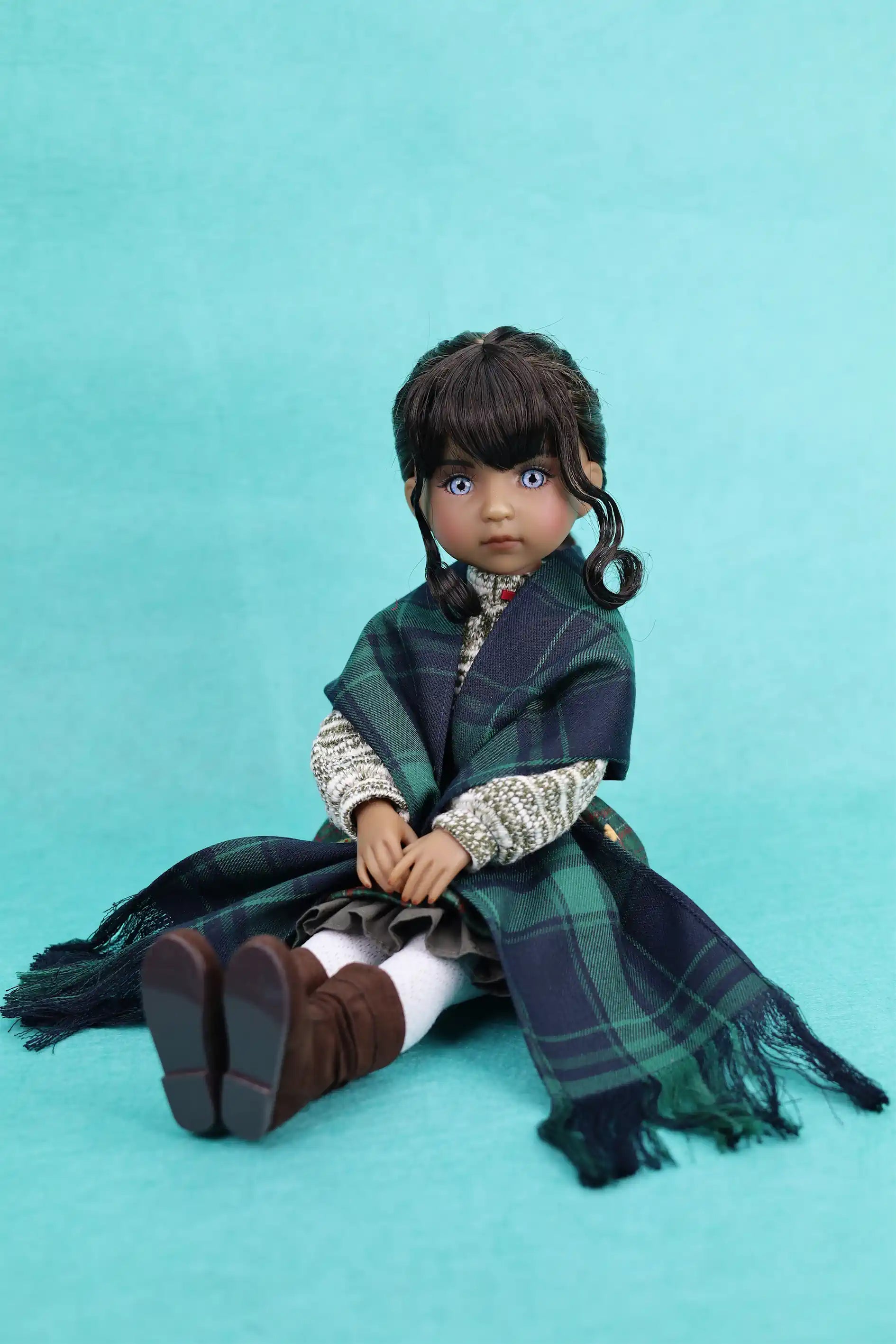 Doll with plaid shawl and braided hair on a teal background