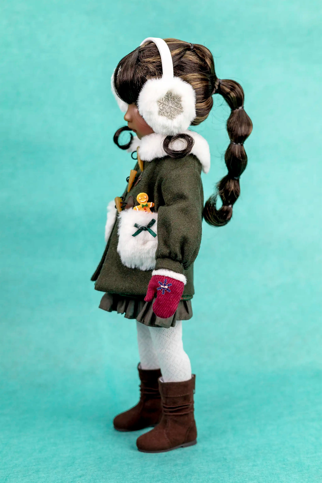 Doll with winter outfit, including a coat, gloves, and headband, on a teal background