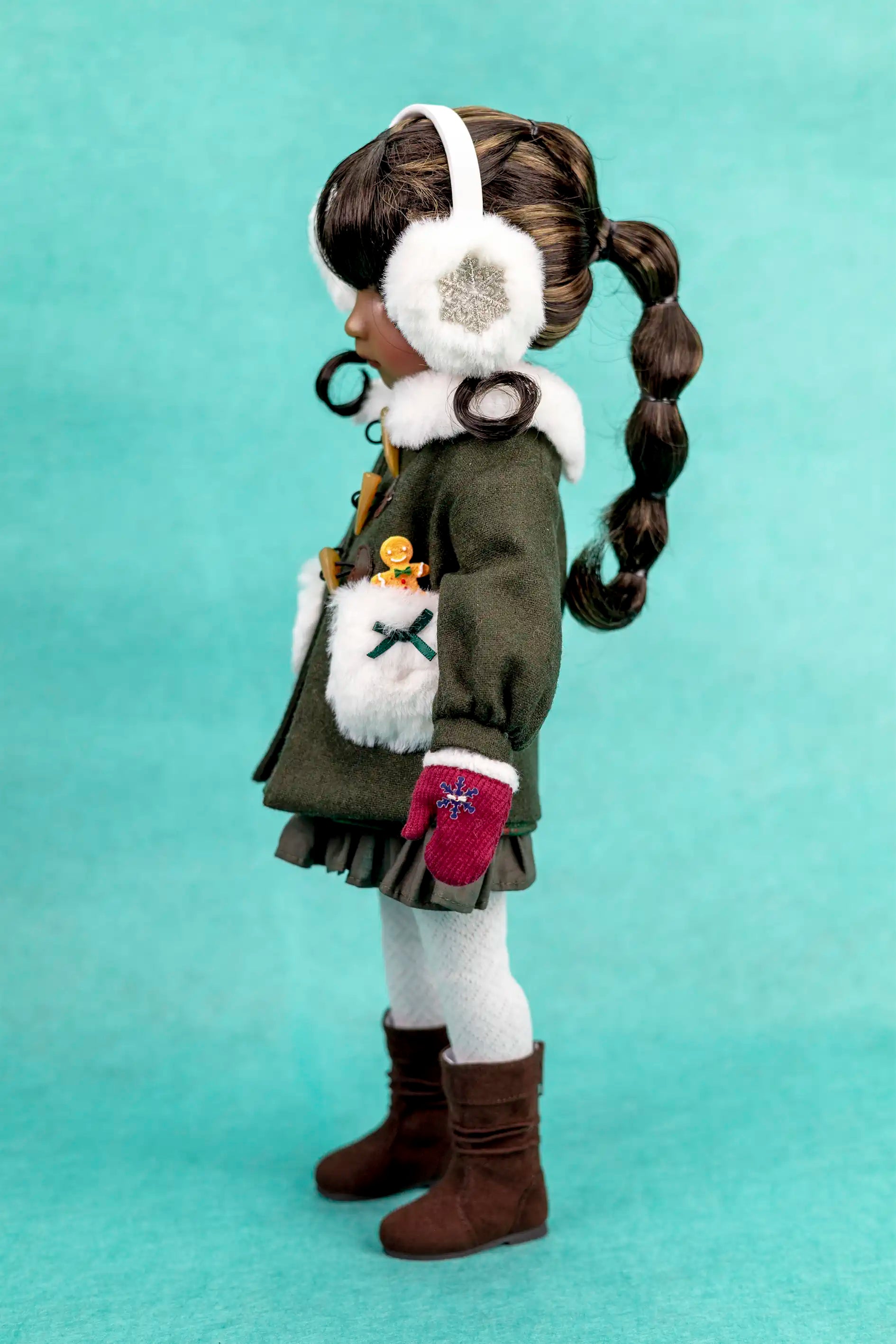 Doll with winter outfit, including a coat, gloves, and headband, on a teal background
