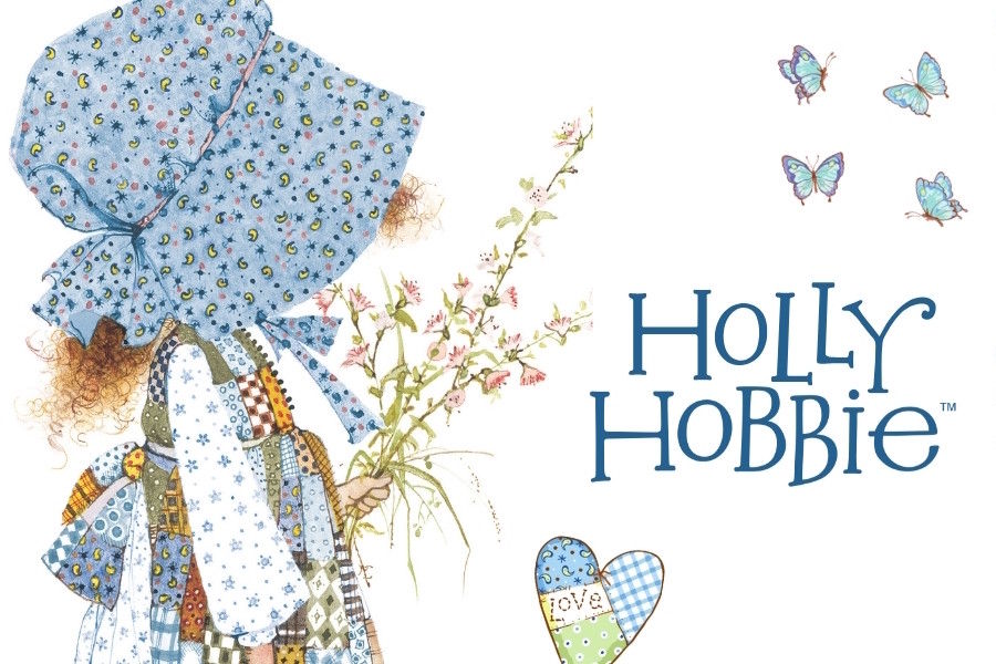 Illustration of a character from Holly Hobbie with a large blue hat and floral dress, holding flowers, on a white background.