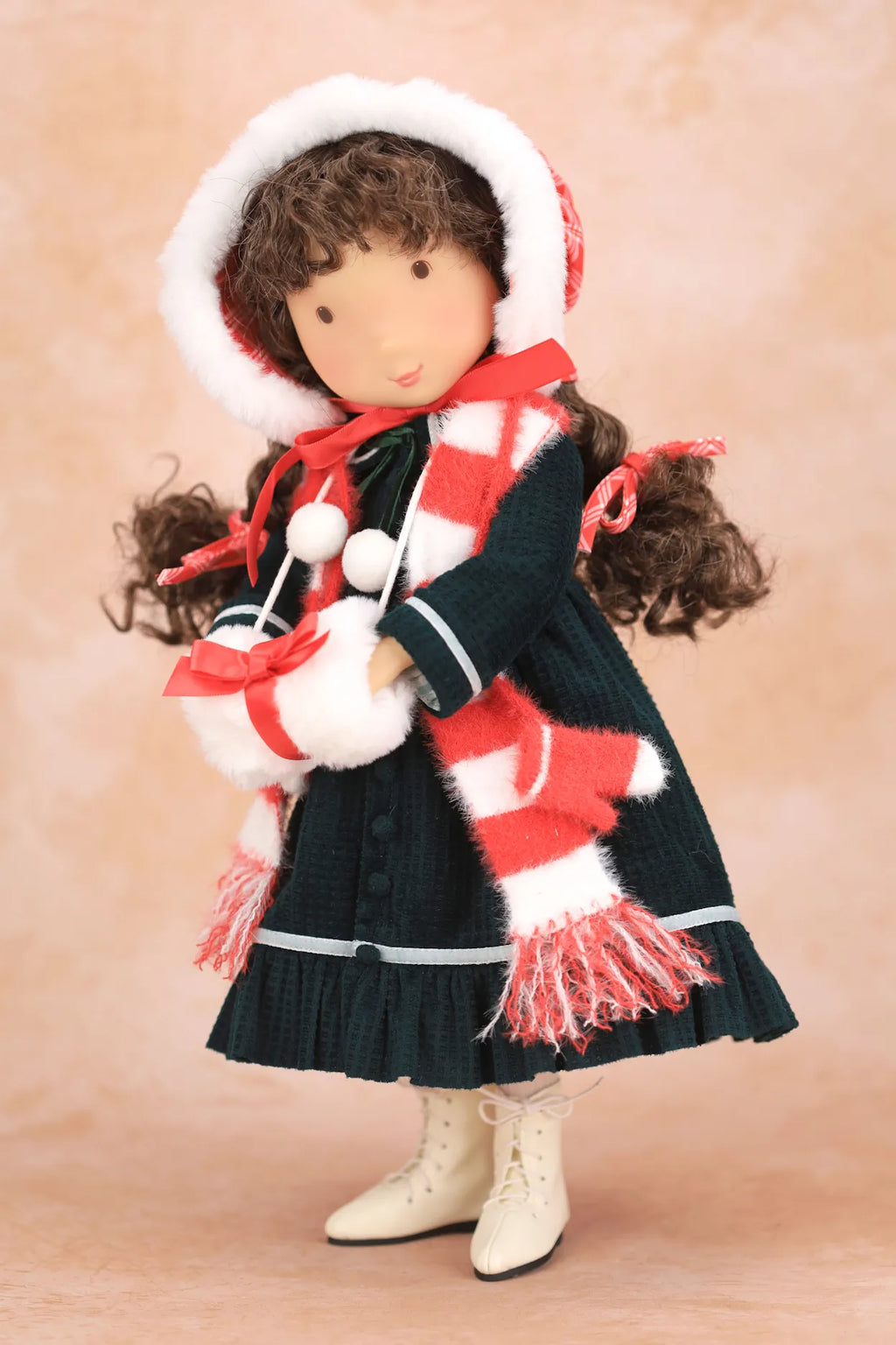 A Holly Hobbie doll dressed in a dark green dress with a red and white striped scarf, a matching red and white striped bonnet with white trim, and cream-colored boots, set against a soft beige background.