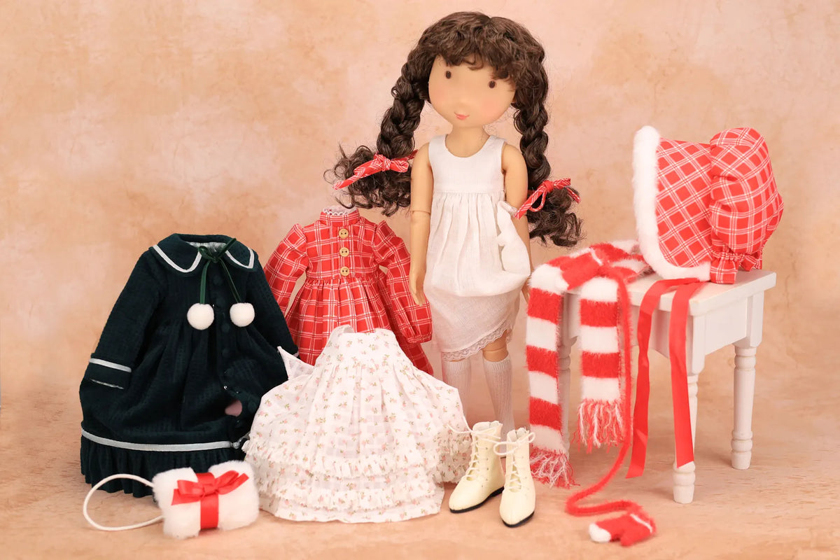 A Holly Hobbie doll with long dark curly hair stands in a styled indoor scene wearing a white dress, surrounded by matching red-and-white and black clothing items including a coat, skirt, scarf, hat, and boots, against a warm beige backdrop.