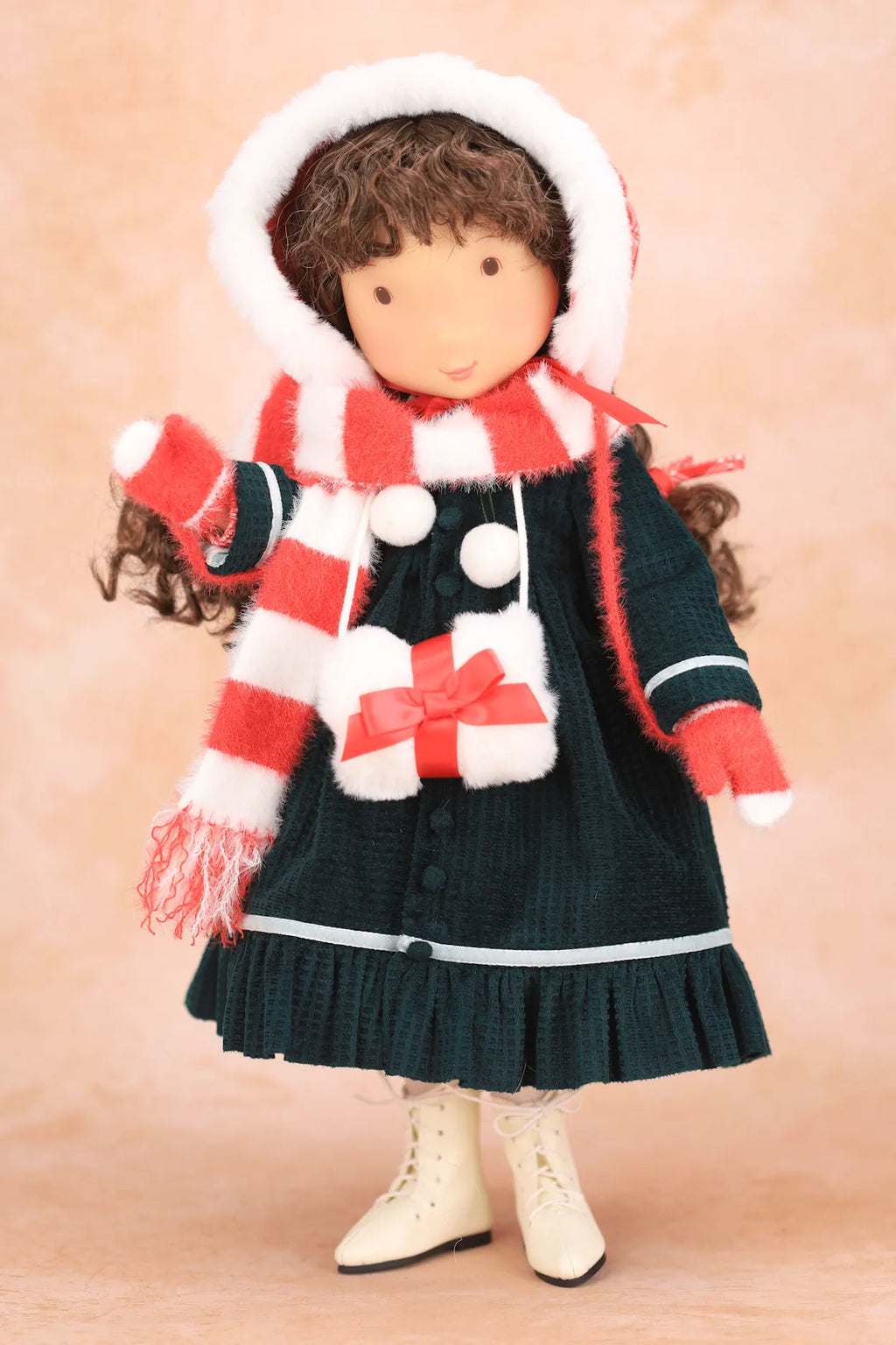 A Holly Hobbie doll dressed in a dark green dress with a red and white striped scarf, a matching red and white striped bonnet with white trim, and cream-colored boots, set against a soft beige background.